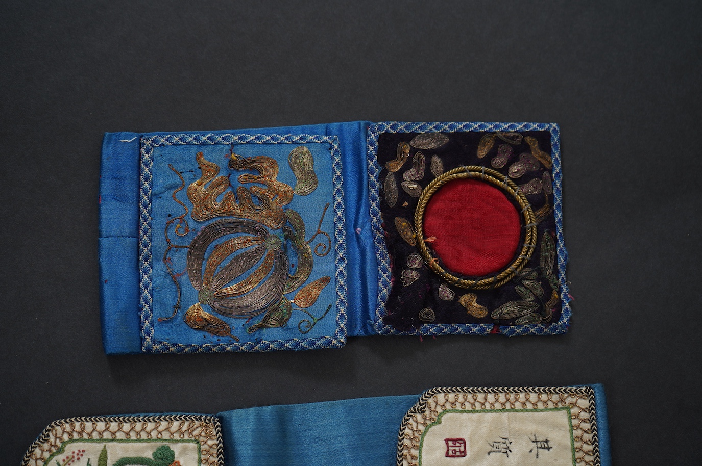 Two Chinese late Qing Dynesty coloured silk and gold thread embroidered belt purses, or ‘hebao’, for carrying coins, seals and fragrant herbs etc. One - 19cm long,in cream silk, with the embroidered words: “It’s music is